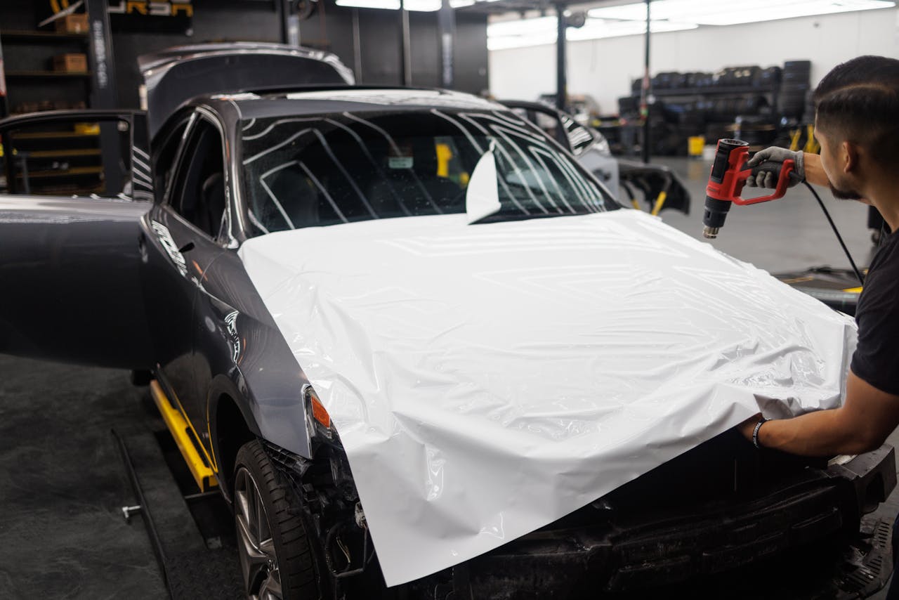 hero-img-01 Car being wrapped with white vinyl in an auto workshop by a skilled mechanic.