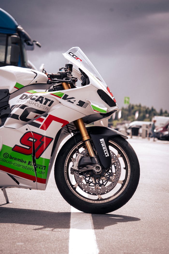 why-choose-us A Ducati racing motorbike parked at Nürburgring on a cloudy day, showcasing vibrant decals and sleek design.